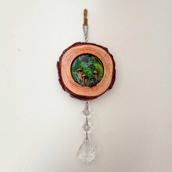 boreal forest suncatcher featuring a round wood slice with bark edge, colorful mushroom scene, dragonfly and clear hanging crystals