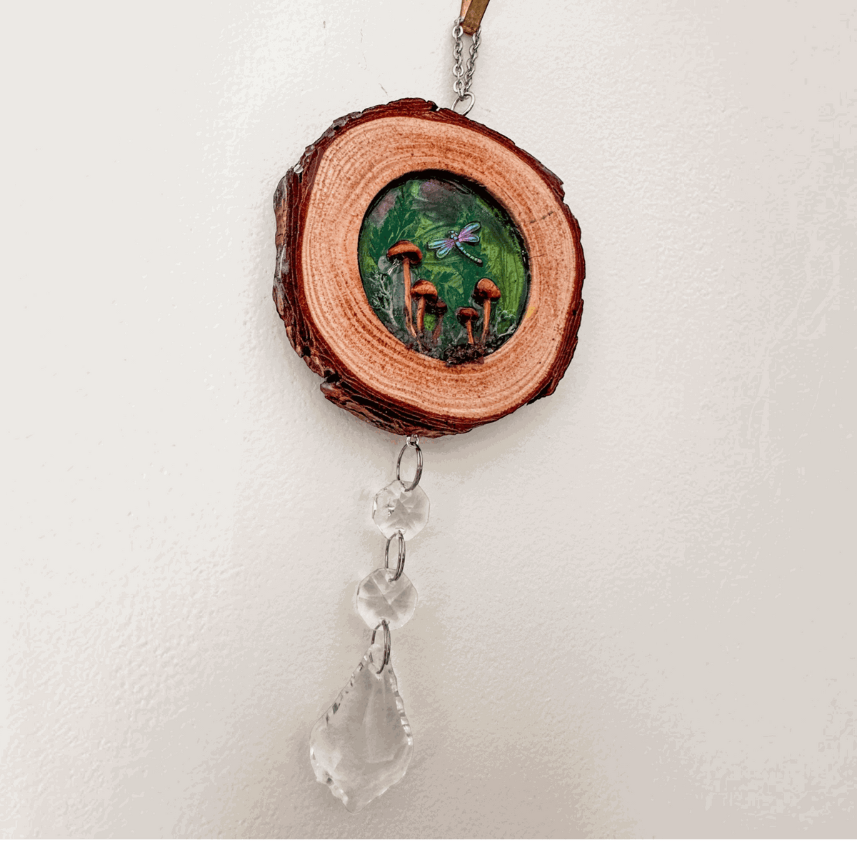 boreal forest suncatcher on a natural bark-edged wood slice, with a green mushroom scene, dragonfly and hanging clear crystals