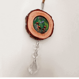 boreal forest suncatcher on a natural bark-edged wood slice, with a green mushroom scene, dragonfly and hanging clear crystals