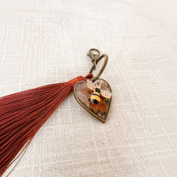 bumble bee resin keychain with an antique bronze heart, honeycomb and pressed flowers, plus a striped bee charm and rust tassel