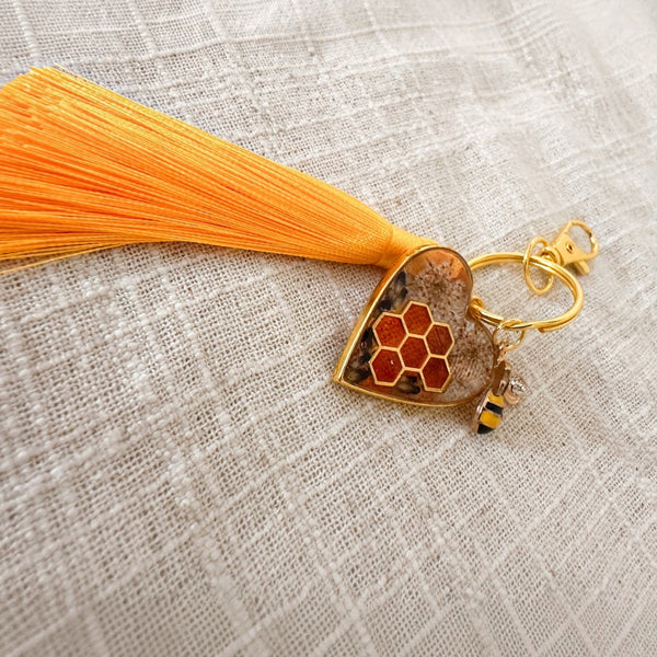 bumble bee resin keychain with a gold heart frame, honeycomb detail, pressed flowers, bee charm and orange tassel