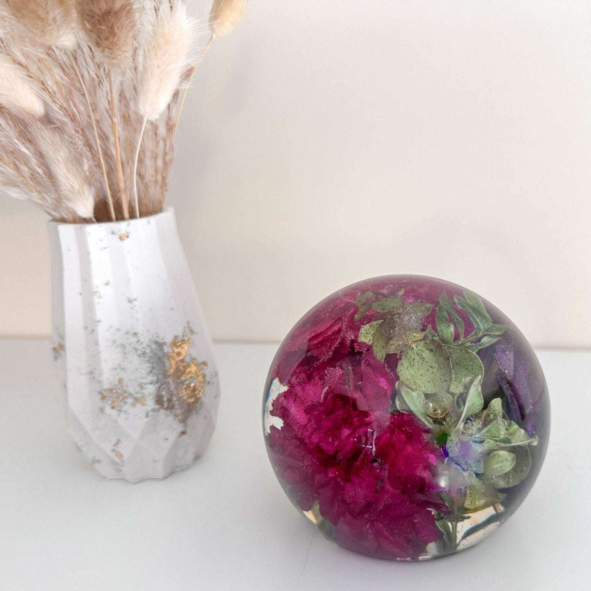 Floral resin sphere with real dark pink and purple carnations and LED light base glowing as decorative garden art