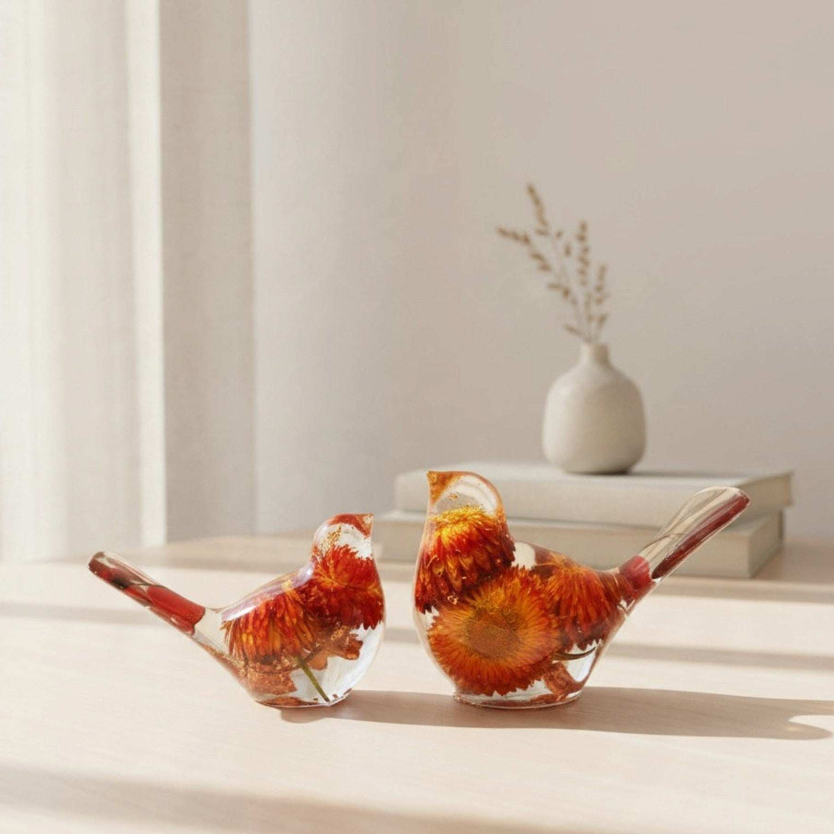 Resin Bird Pair with clear resin bodies, vivid orange and red dried flowers, and slender red botanical tails.