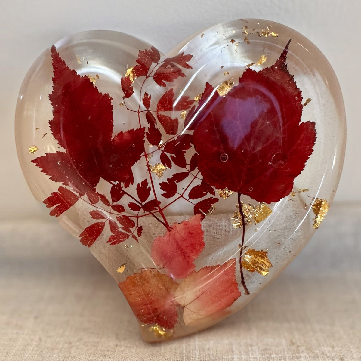 Red maple leaf resin tray in a heart shape, clear glossy resin with crimson and blush leaves and scattered gold flakes.
