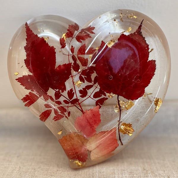 Red maple leaf resin tray in a heart shape, clear glossy resin with crimson and blush leaves and scattered gold flakes.