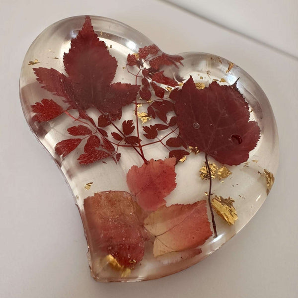 Red maple leaf resin tray in a clear glossy heart shape, preserving crimson and blush foliage with scattered gold leaf flakes.