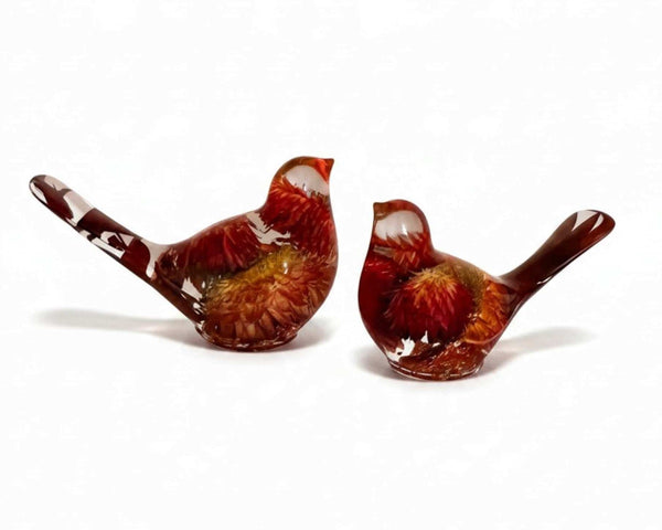 Resin Bird Pair with clear amber-toned resin, deep red and orange dried flowers, and long, tapered tails.