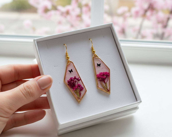 Handcrafted geometric gold-framed pink butterfly resin earrings with pink flowers and a butterfly.