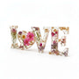 Wildflower resin word art spelling LOVE with pink daisies, white daisy, purple wildflowers, rose buds, greenery, and gold leaf flakes