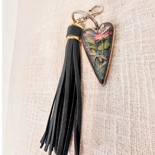dragonfly resin keychain with a glossy dark heart pendant, pressed pink flower, green leaves, colourful dragonfly and black tassel