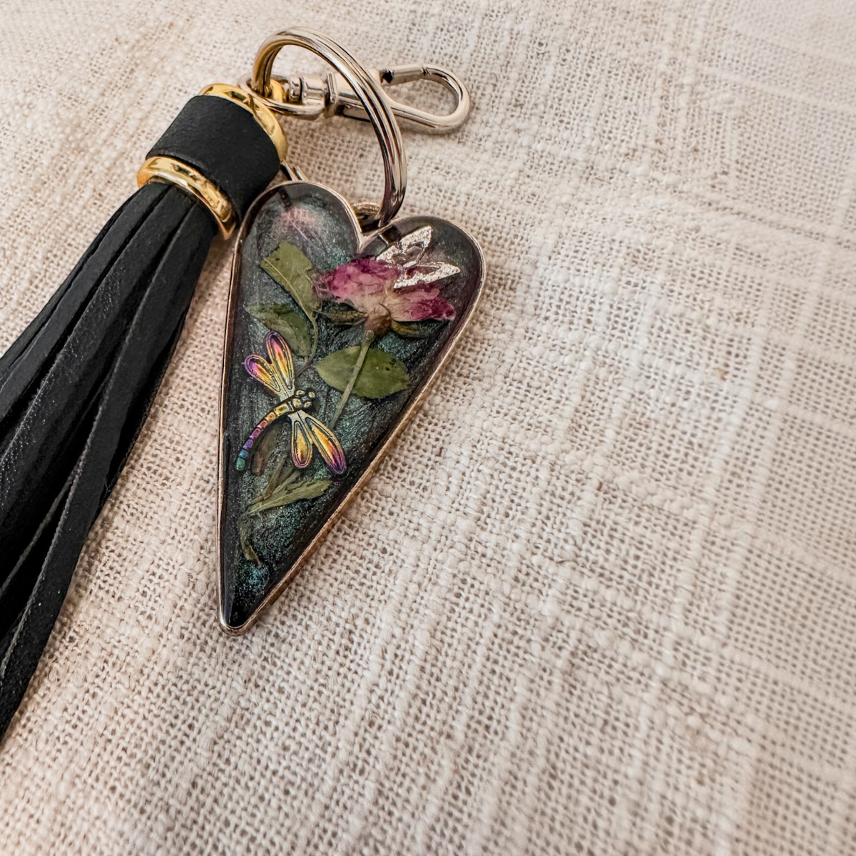 dragonfly resin keychain with a glossy dark heart, pressed pink rose and green leaves, colorful dragonfly, and black leather tassel