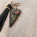 dragonfly resin keychain with a glossy dark heart, pressed pink rose and green leaves, colorful dragonfly, and black leather tassel