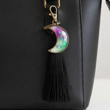 Glow in the dark moon keychain with a pink and green marbled crescent, star details, bronze frame and black tassel