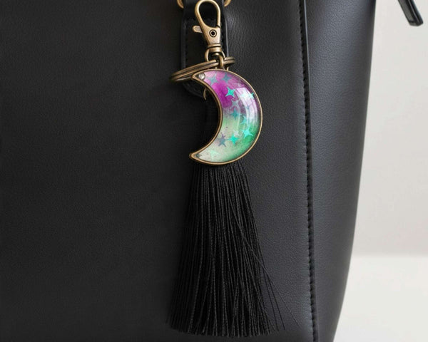 Glow in the dark moon keychain with a pink and green marbled crescent, star details, bronze frame and black tassel