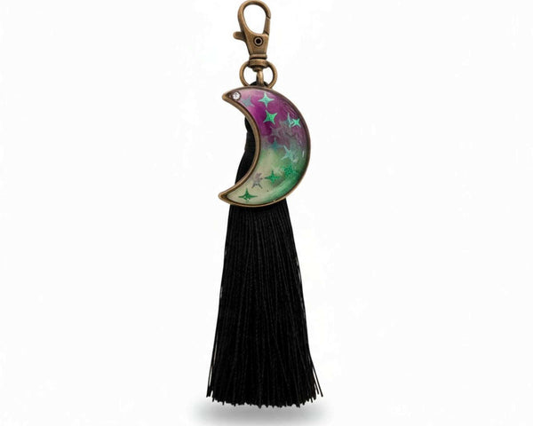 Glow in the dark moon keychain with a pink and green swirled resin crescent, star details, bronze clasp and black tassel
