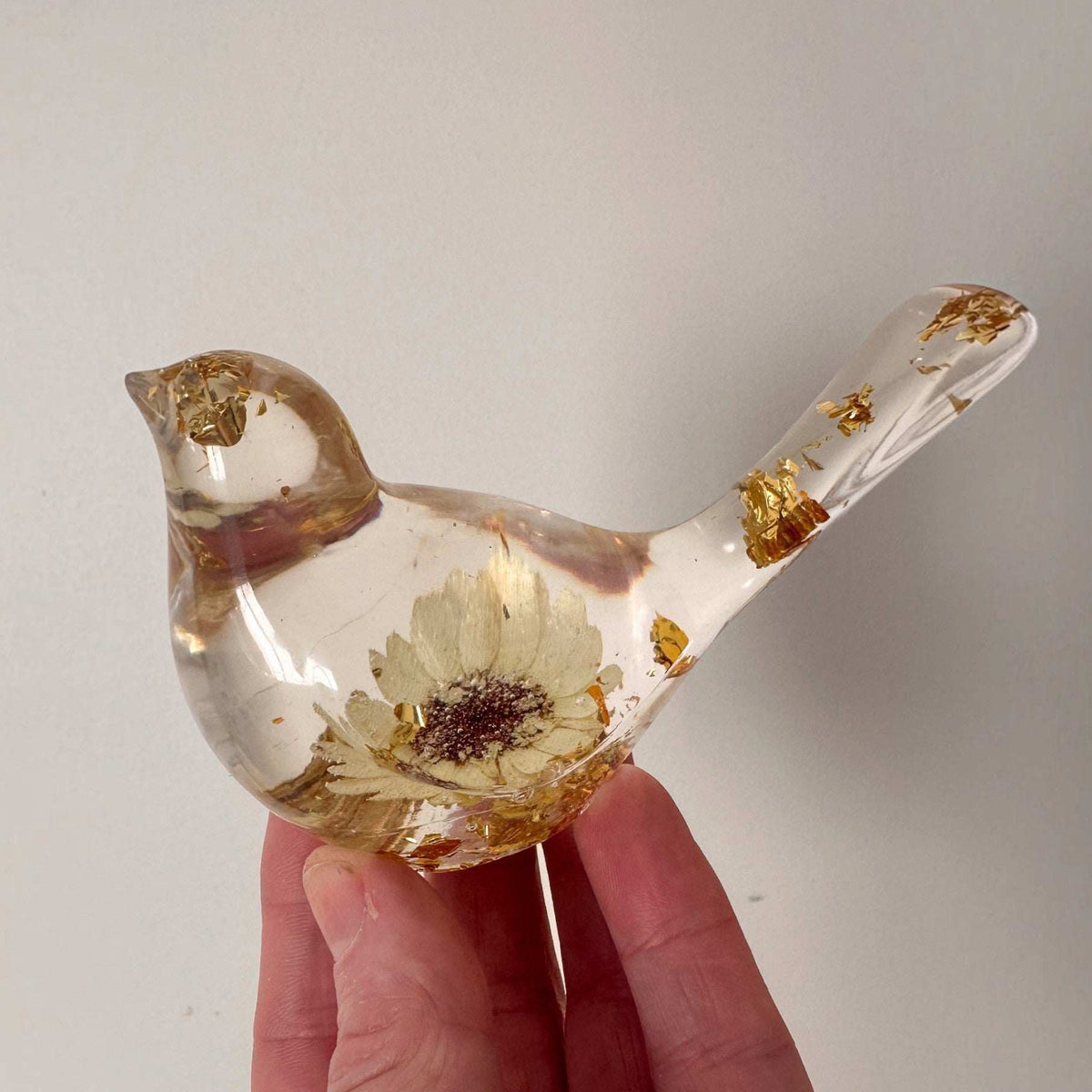 Gold leaf resin bird held in a hand against a snowy sunset