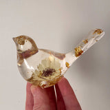 Gold leaf resin bird held in a hand against a snowy sunset