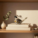 Handmade chickadee resin bird sitting on a shelf beside a houseplant