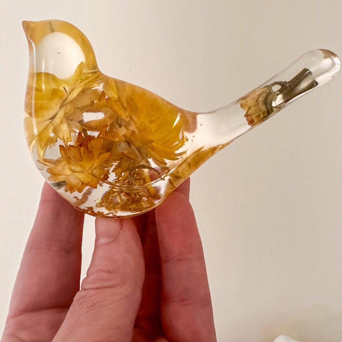 Yellow Strawflower Resin Bird with amber dried petals embedded in clear resin, a transparent head and bud-filled tail.
