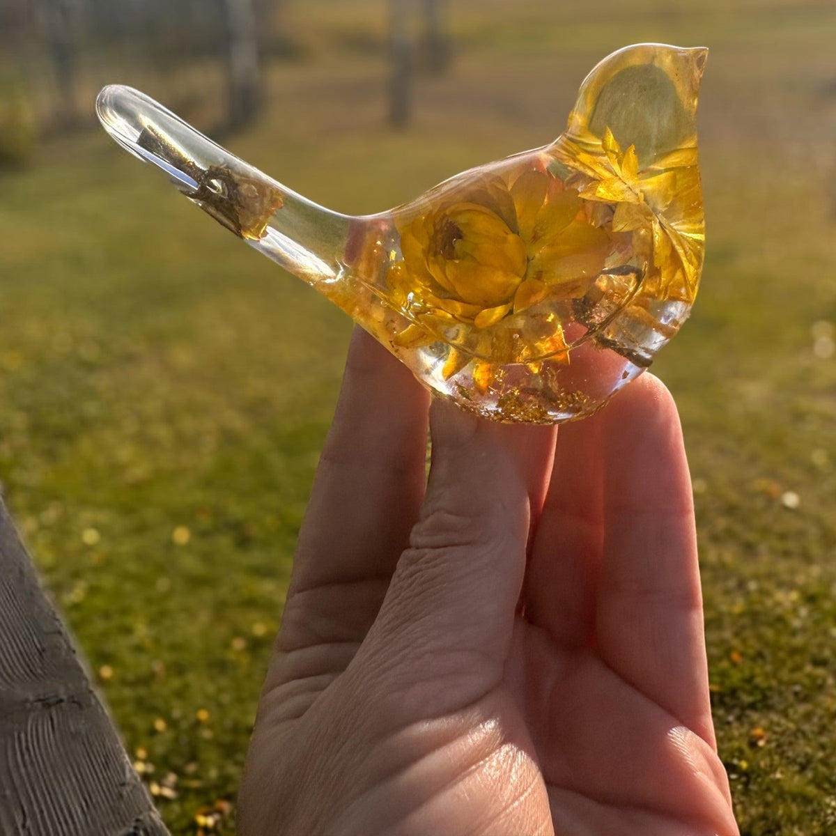 Yellow Strawflower Resin Bird in clear amber resin, with golden dried flowers, a transparent beak and tail, and gold flecks at the base.