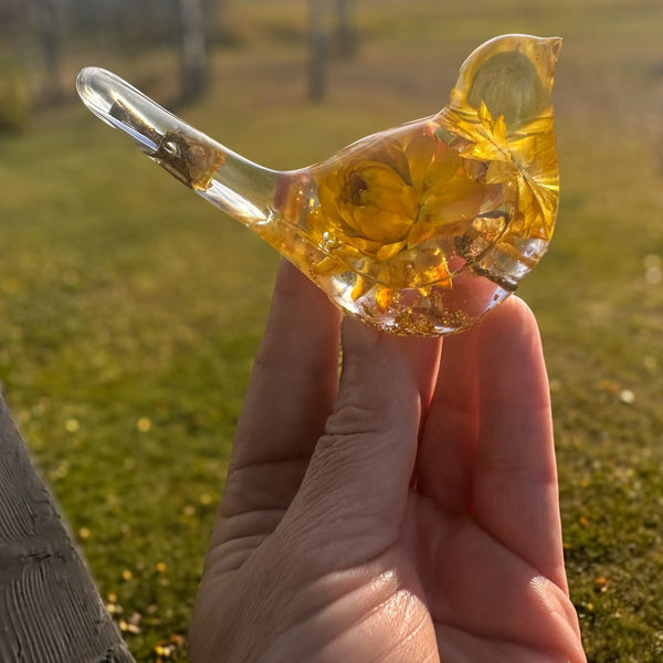 Yellow Strawflower Resin Bird in clear amber resin, with golden dried flowers, a transparent beak and tail, and gold flecks at the base.