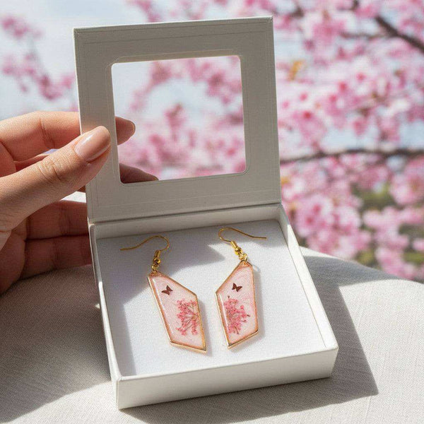Handcrafted geometric gold-framed pink butterfly resin earrings with pink flowers and a butterfly.