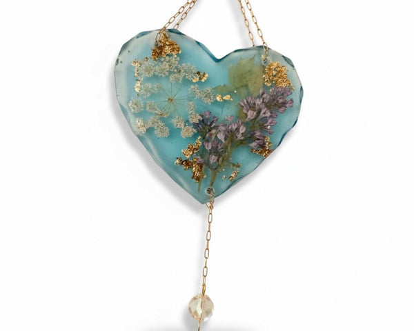 Glow in the dark heart suncatcher with blue resin, real pressed lilac and white wildflowers, gold leaf accents, and hanging crystal drop.