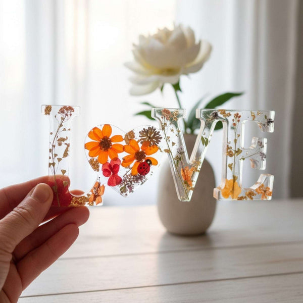 Pressed flower resin decor spelling LOVE with real wildflowers and a tiny ladybug in clear resin letters