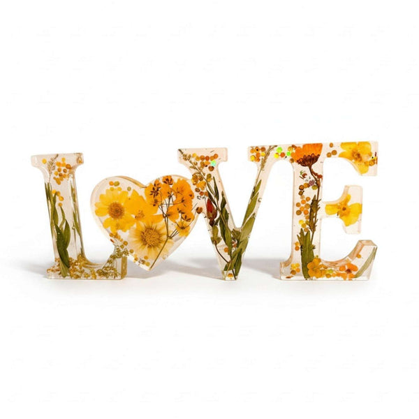 Pressed flower resin love sign in clear resin, spelling LOVE with yellow wildflowers and a floral heart-shaped O