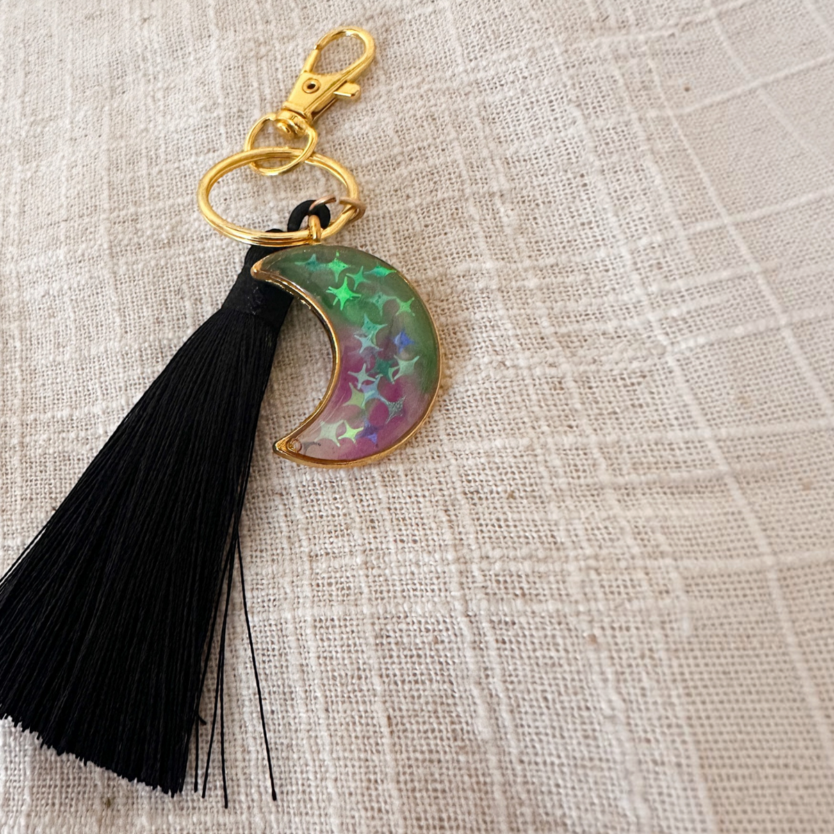 Luna Glow crescent moon keychain in translucent pink and green swirled resin with star details, gold hardware and black tassel