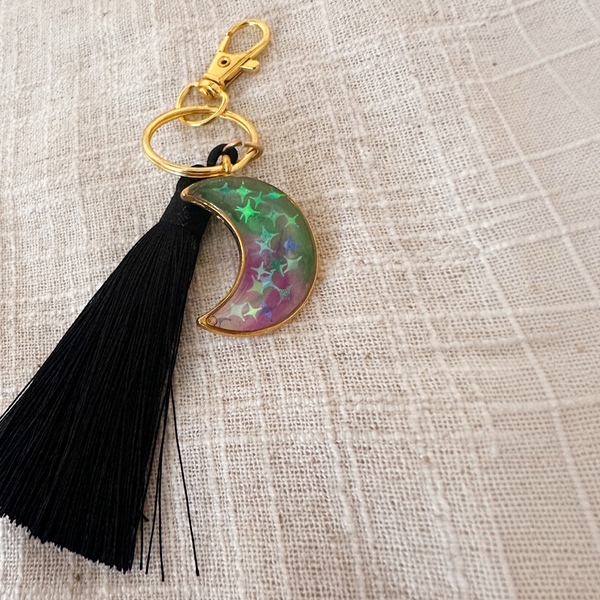 Luna Glow crescent moon keychain in translucent pink and green swirled resin with star details, gold hardware and black tassel