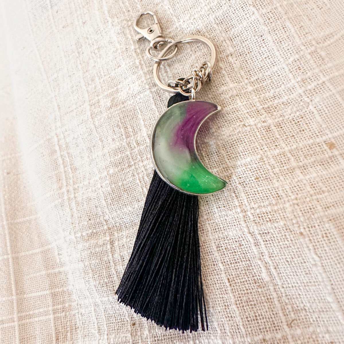 Luna Glow crescent moon keychain in translucent resin with purple and green swirls, silver hardware and a black tassel