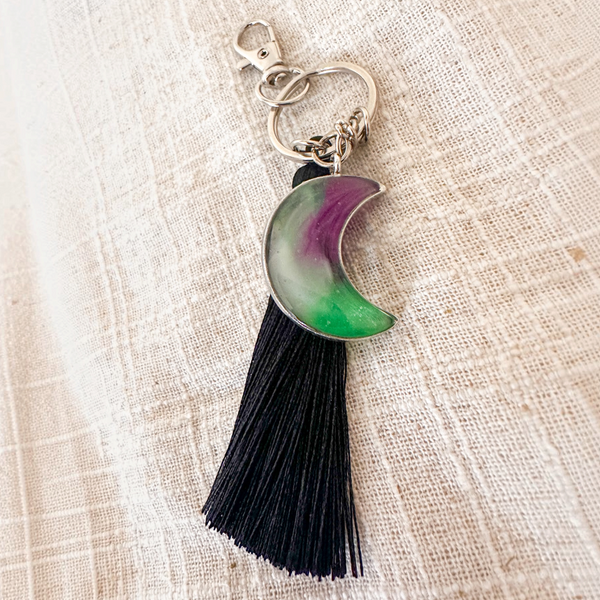 Luna Glow crescent moon keychain in translucent resin with purple and green swirls, silver hardware and a black tassel
