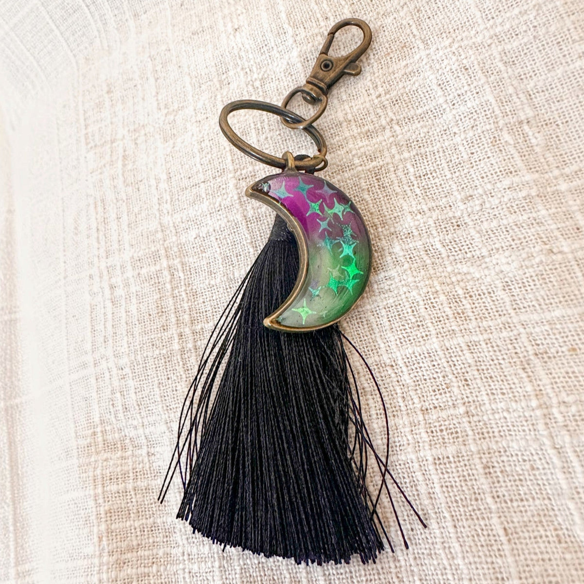 Luna Glow crescent moon keychain in pink and green swirled resin with star details, bronze hardware and black tassel