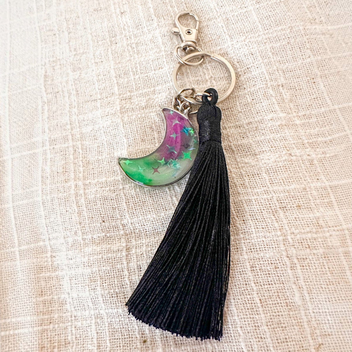 Luna Glow crescent moon keychain in clear resin with pink and green swirls, glowing stars, silver clasp and black tassel