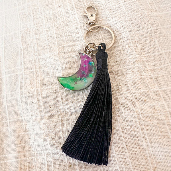 Luna Glow crescent moon keychain in clear resin with pink and green swirls, glowing stars, silver clasp and black tassel