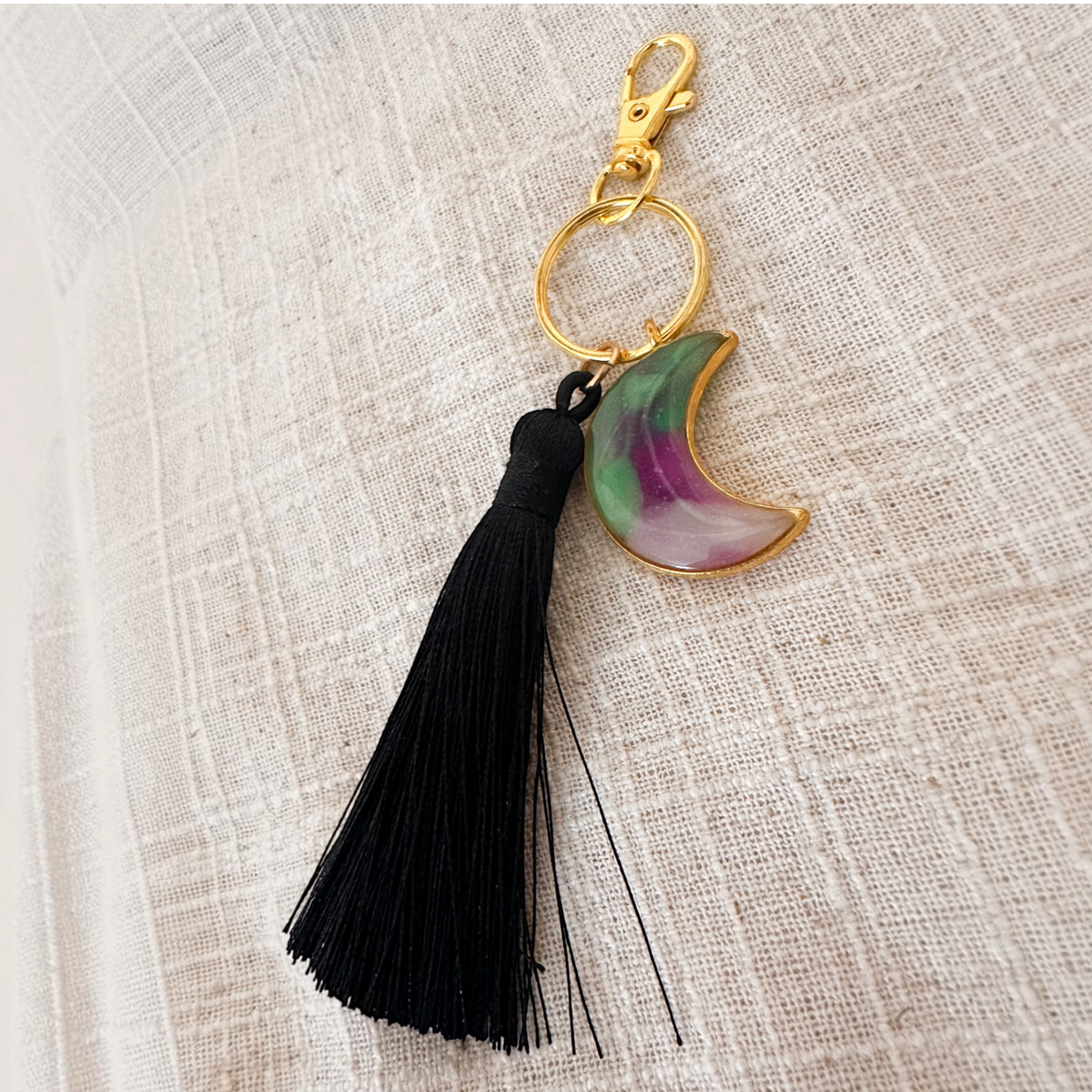 Luna Glow moon keychain in translucent resin with purple and green swirls, gold hardware and a long black tassel