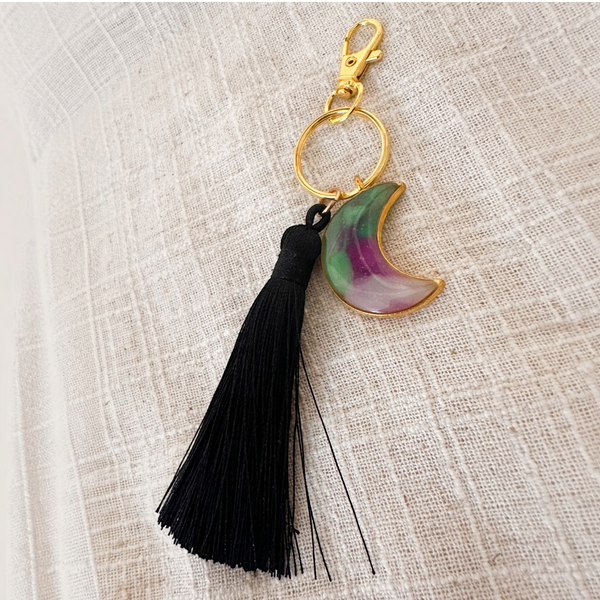 Luna Glow moon keychain in translucent resin with purple and green swirls, gold hardware and a long black tassel
