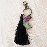 Luna Glow crescent moon keychain in translucent purple and green swirled resin, with an antique bronze clasp and black tassel