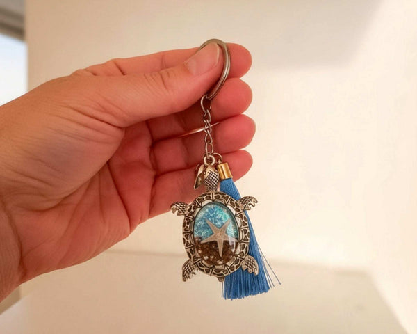 Sea turtle keychain in antique bronze metal with a blue tassel and oval resin center featuring a starfish and ocean tones.