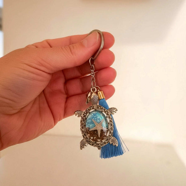 Sea turtle keychain in antique bronze metal with a blue tassel and oval resin center featuring a starfish and ocean tones.