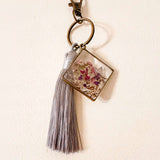 Meadow Butterfly bag charm with pressed pink and purple flowers in clear resin, bronze frame and grey tassel