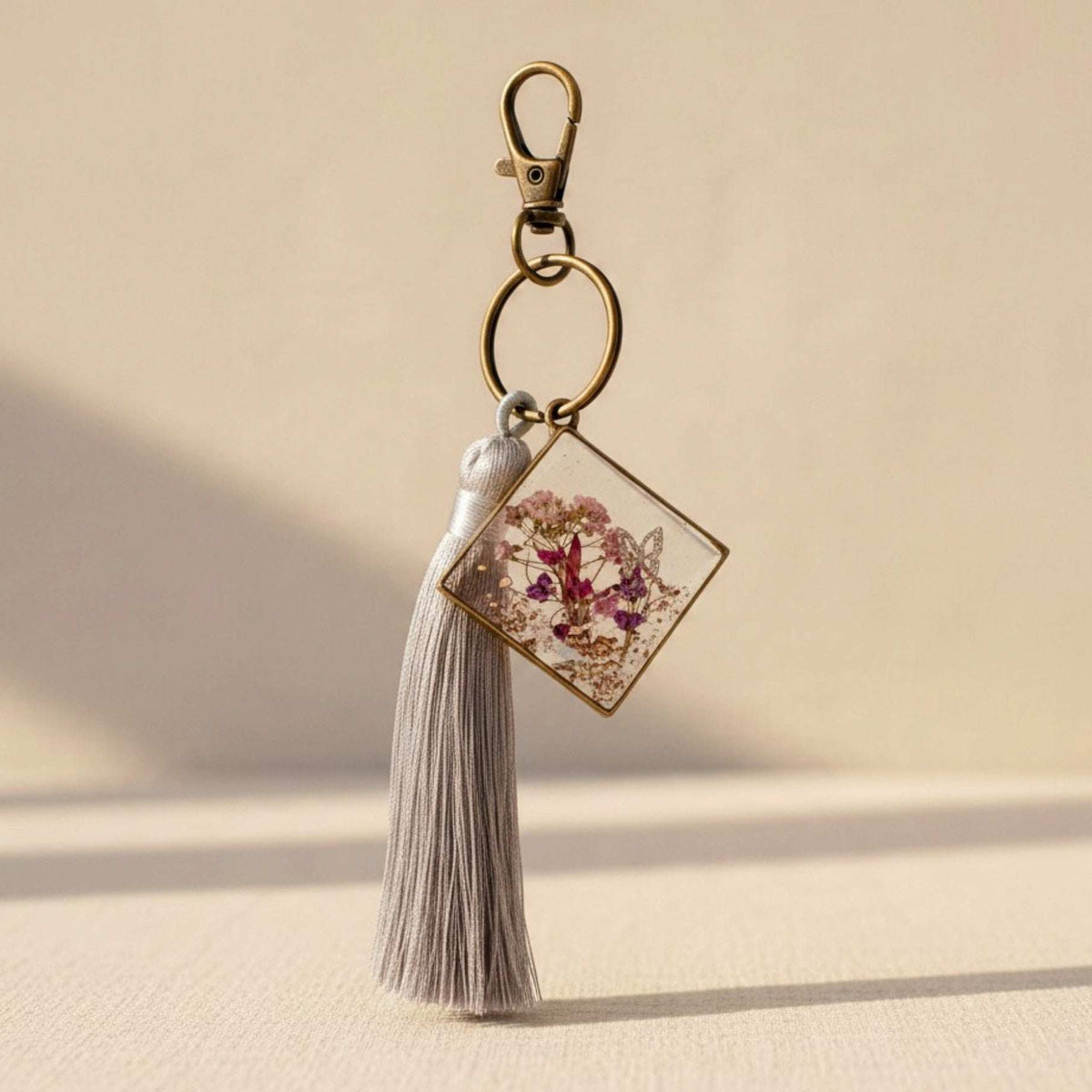 Meadow Butterfly pressed flower bag charm in a bronze square frame with pink and purple blooms and a grey tassel
