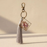 Meadow Butterfly pressed flower bag charm in a bronze square frame with pink and purple blooms and a grey tassel