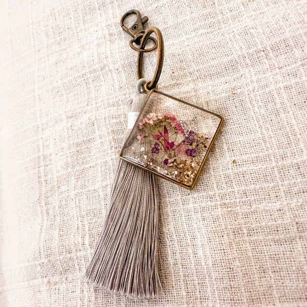 Meadow Butterfly pressed flower bag charm in clear resin, with pink and purple blooms, bronze frame and grey tassel