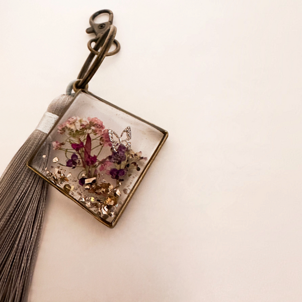 Meadow Butterfly pressed flower resin bag charm with pink and purple blooms, gold flakes, bronze frame and grey tassel