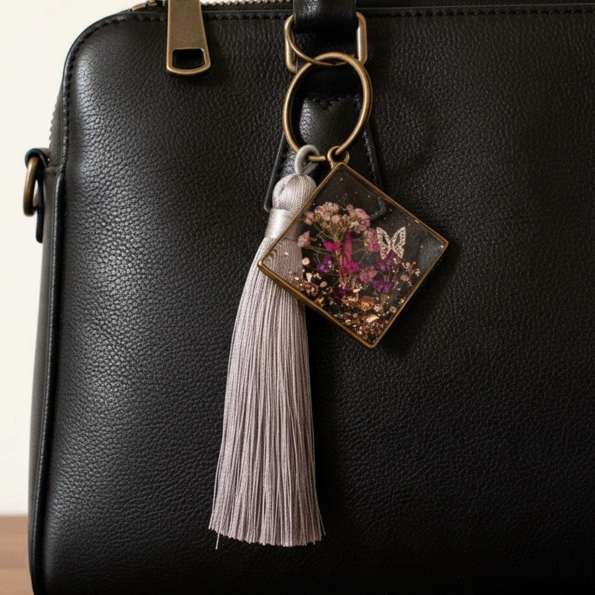 Meadow Butterfly bag charm with pressed pink and purple flowers in clear resin, bronze frame and grey tassel