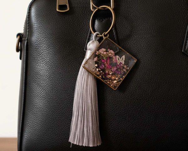 Meadow Butterfly bag charm with pressed pink and purple flowers in clear resin, bronze frame and grey tassel