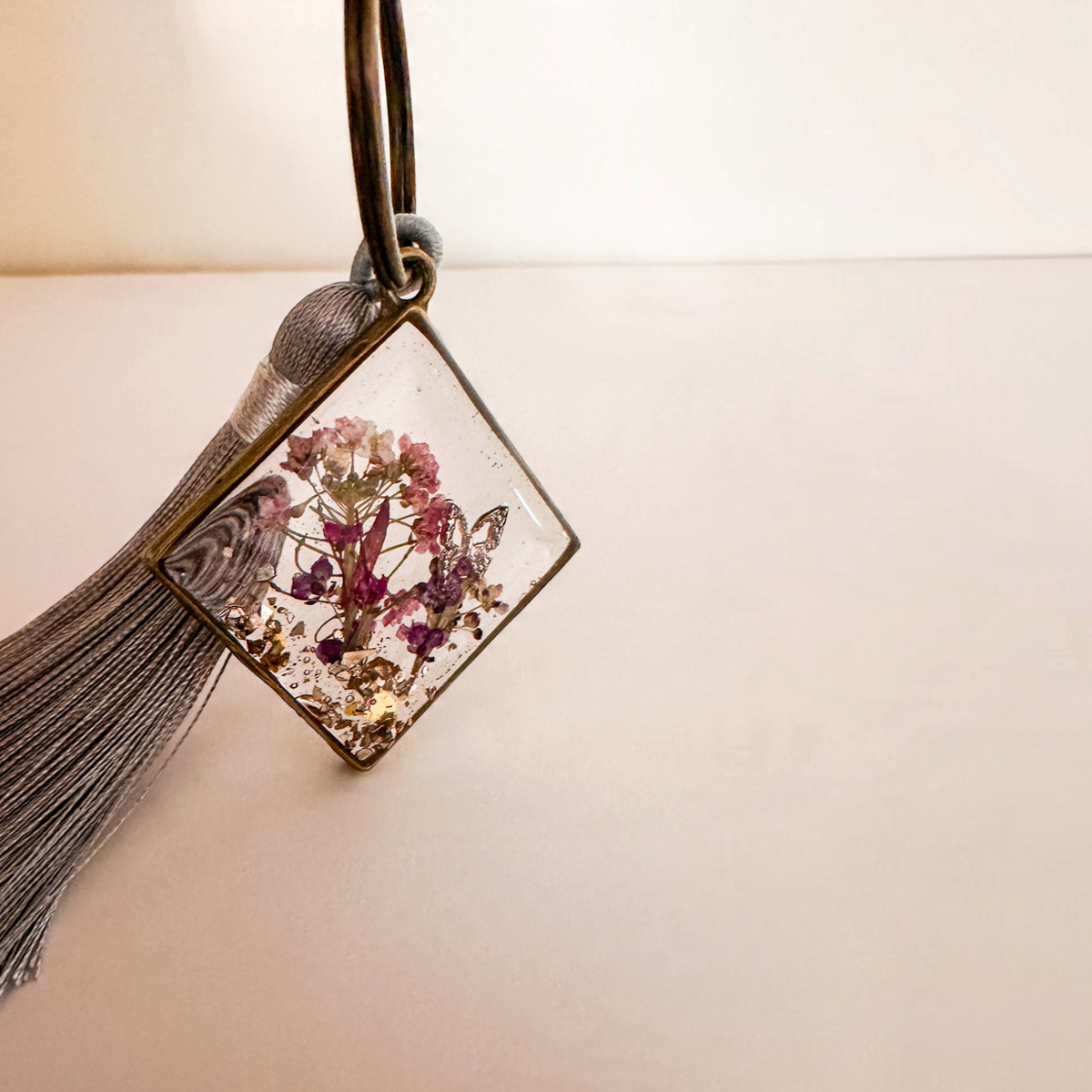 Meadow Butterfly resin bag charm with pressed pink and purple flowers in a bronze frame and grey tassel
