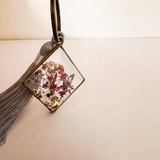 Meadow Butterfly resin bag charm with pressed pink and purple flowers in a bronze frame and grey tassel